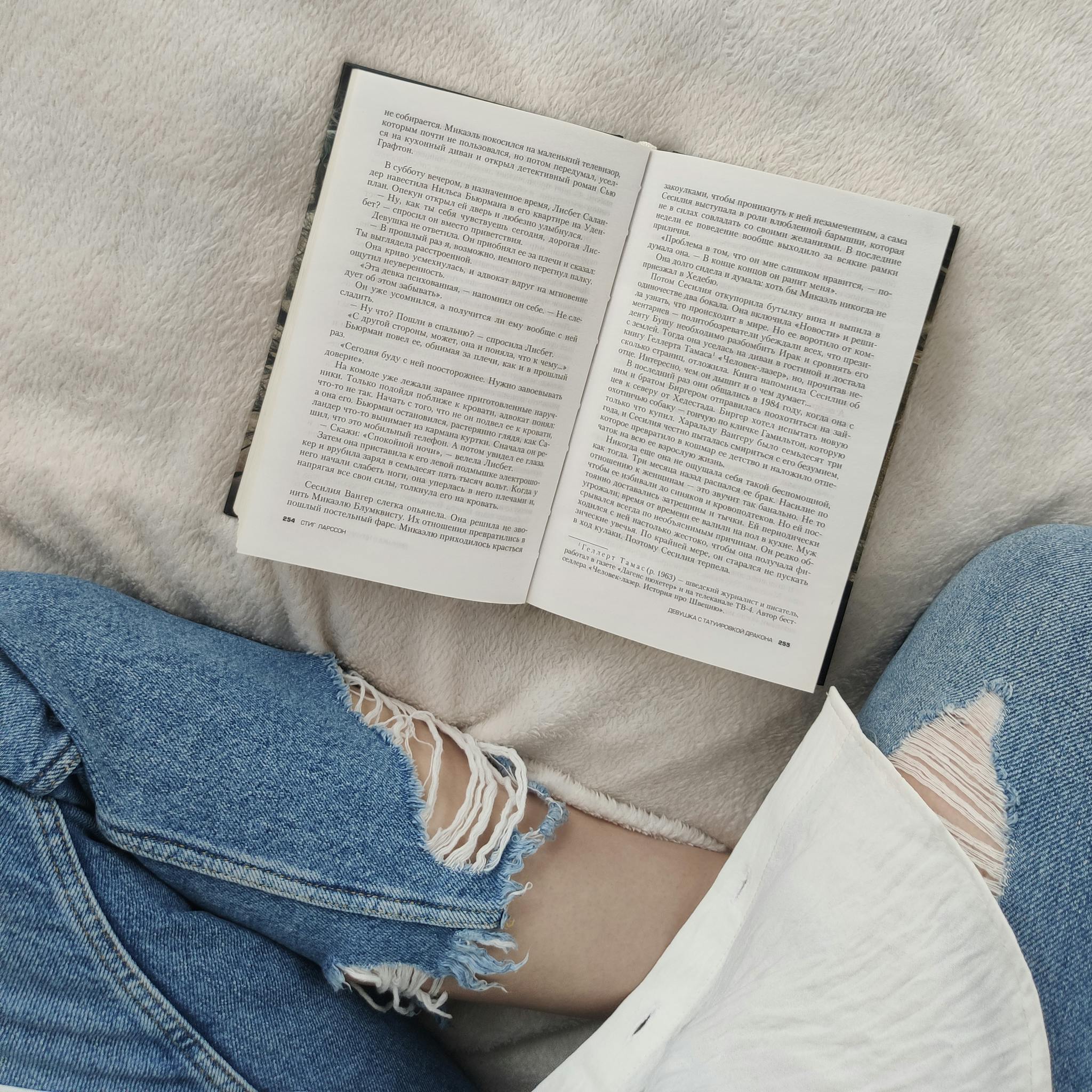 Top view crop anonymous female wearing casual outfit sitting on comfortable soft bed with legs crossed and reading good book in free time